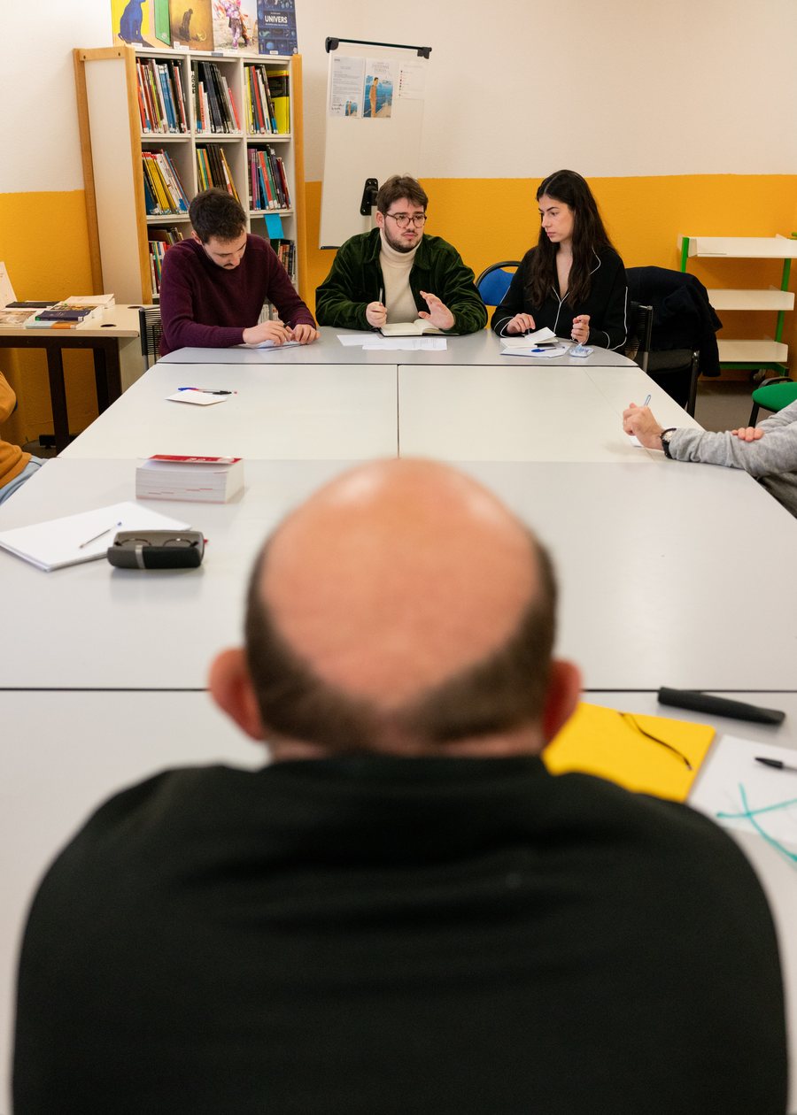 Trois formateurs bénévoles face à une personne détenue, lors d'un atelier d'éloquence dans la bibliothèque du centre pénitentiaire.
